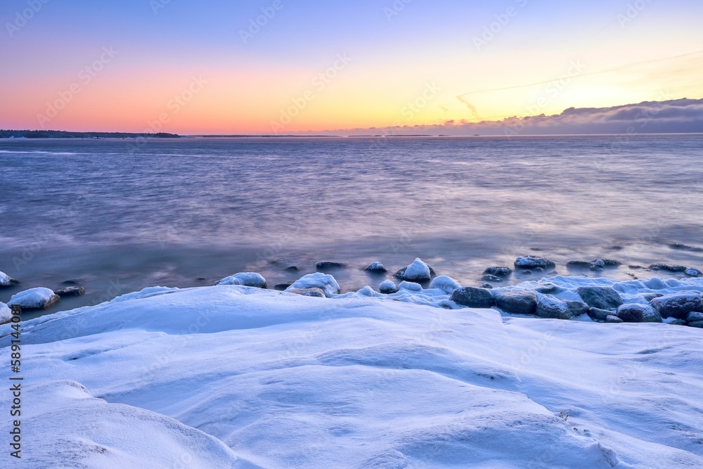 Scenic view of a beautiful sunrise with a snow-covered beach next to the water Scenic view of a beautiful sunrise with a snow-covered beach next to the water