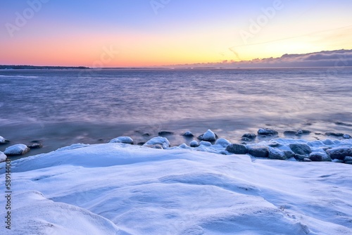 Scenic view of a beautiful sunrise with a snow-covered beach next to the water © Pekka/Wirestock Creators