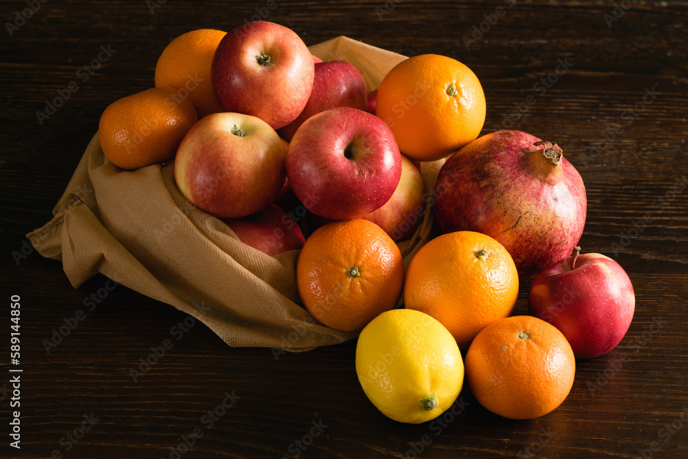 Fruit in a reusable bag. Earth day and zero waste concept. Apples, lemon, oranges and pomegranate on a dark wooden background. Fruit in a reusable bag. Earth day and zero waste concept. Apples, lemon, oranges and pomegranate on a dark wooden background.