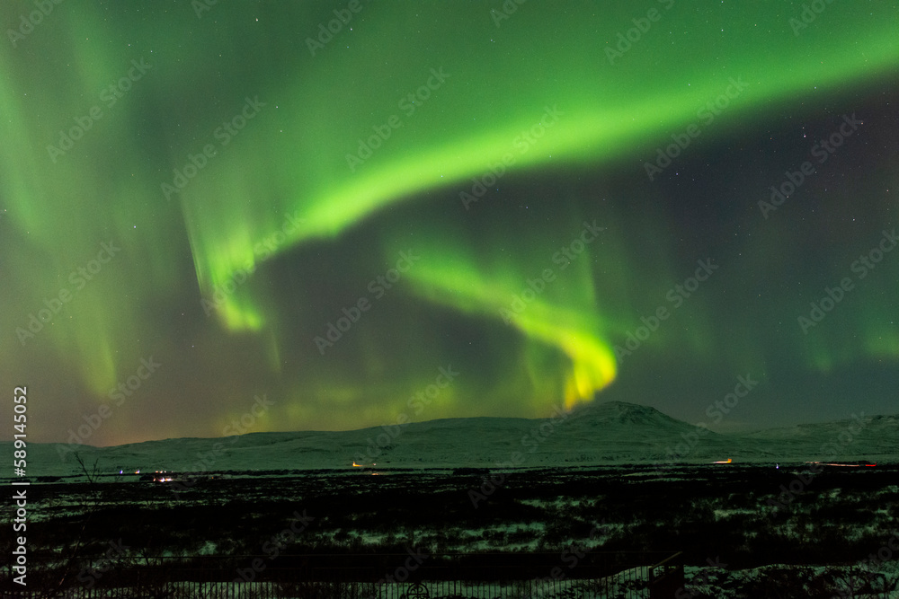 imagen de un paisaje nevado nocturno con montañas al fondo y una aurora boreal sobre el cielo de Islandia 