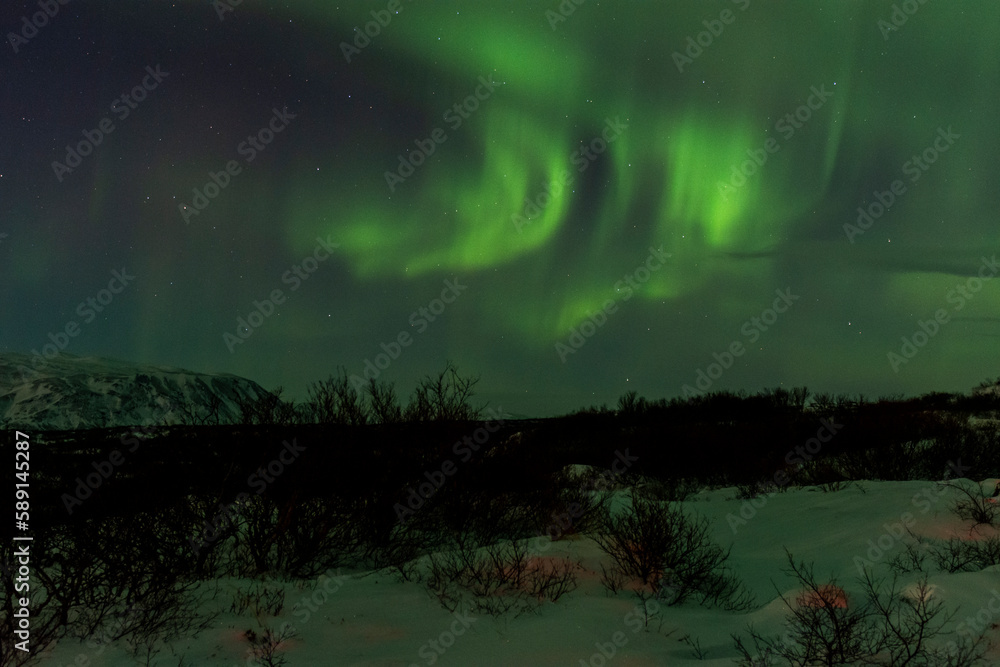 imagen de un paisaje nocturno nevado, con montañas de fondo, y una aurora boreal sobre el cielo de Islandia 