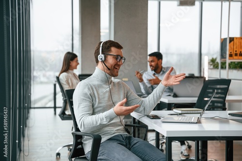 Having a call. In headphones. Men and woman are working in the office together