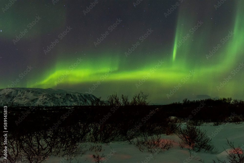 imagen de un paisaje nocturno nevado con montañas al fondo y una aurora boreal en el cielo de Islandia 