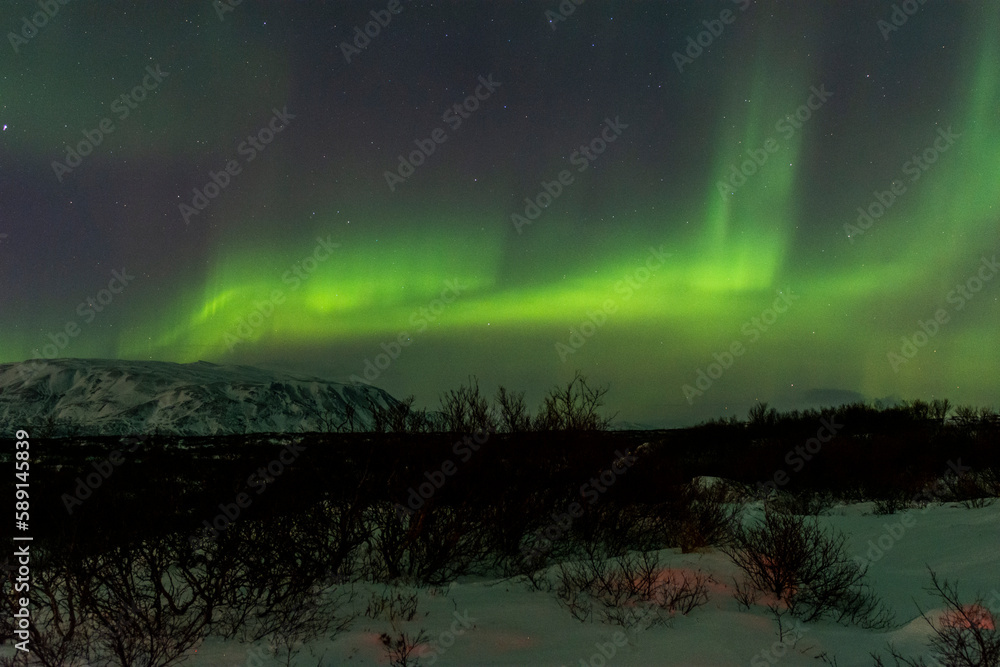 imagen de un paisaje nocturno nevado con las montañas de fondo y una aurora boreal en el cielo de Islandia 