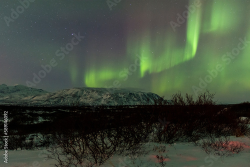 imagen de un paisaje nocturno nevado con las montañas de fondo y una aurora boreal en el cielo de Islandia 
