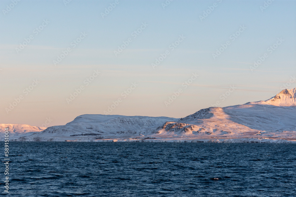 imagen de un paisaje de montañas nevadas, con el cielo azul, visto des del mar 