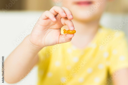 Child hand holding fish oil capsule on white background. Omega 3, fish fat capsule in kid's hand. Children's health care concept.