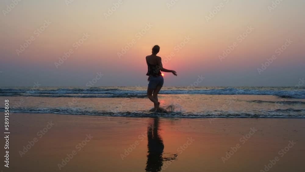 Happy woman dancing in waves on the seacoast at sunset. Silhouette of young female tourist having fun during summer vacation on the sea. Happy woman dancing in waves on the seacoast at sunset. Silhouette of young female tourist having fun during summer vacation on the sea.