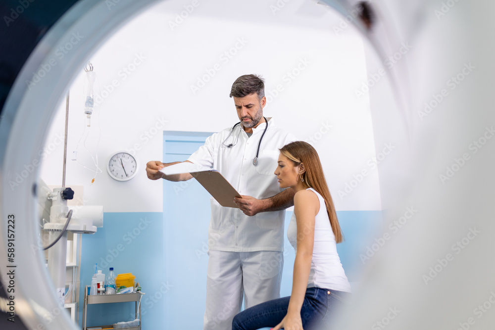 Young medical technician talking to his patient sitting on the CT scanner bed. Young medical technician talking to his patient sitting on the CT scanner bed.