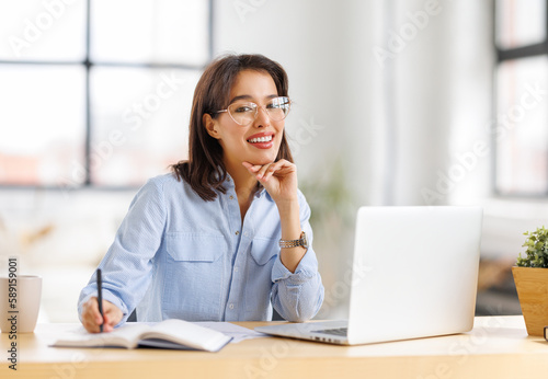 beautiful young smiling woman working remotely behind laptop at home.