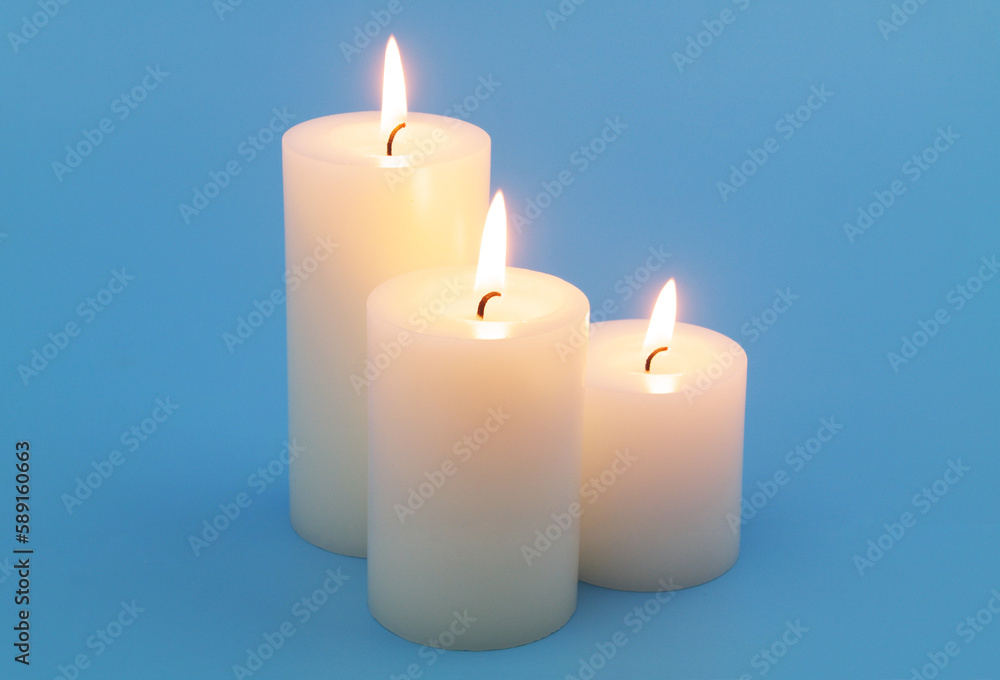 Three candles with different size burning on blue background close-up. Three candles with different size burning on blue background close-up.