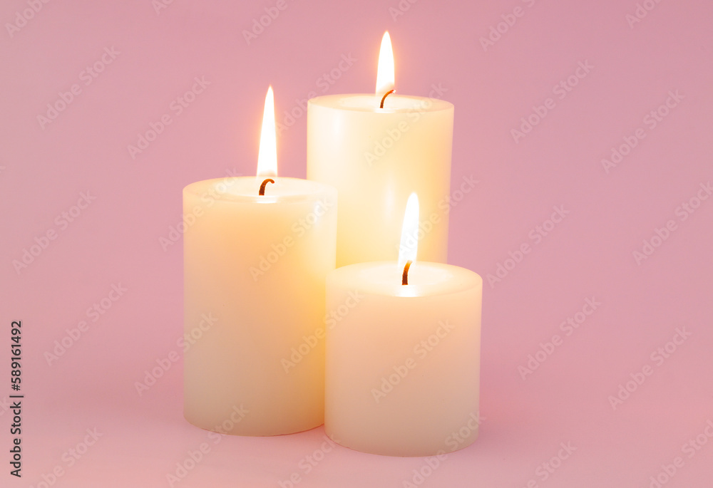 Three white candles with different size burning on pink. Three white candles with different size burning on pink.