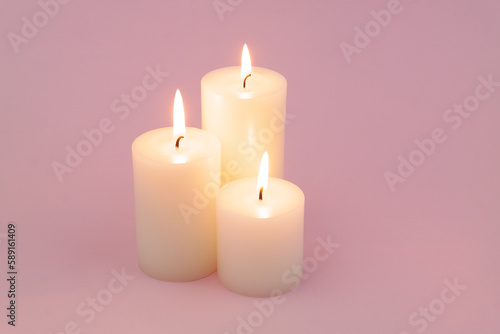 Candles with different size melting and burning on pink background. 