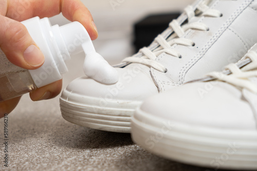 Applying cleaning foam from the bottle to white leather women's sneakers. Care for leather shoes, surface whitening photo