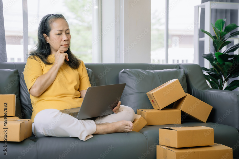 Startup small business entrepreneur or freelance older woman using a laptop with box, checking orders from customers, online marketing delivery, SME Startup small business entrepreneur or freelance older woman using a laptop with box, checking orders from customers, online marketing delivery, SME