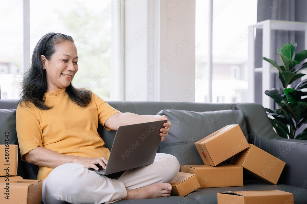 Startup small business entrepreneur or freelance older woman using a laptop with box, checking orders from customers, online marketing delivery, SME Startup small business entrepreneur or freelance older woman using a laptop with box, checking orders from customers, online marketing delivery, SME