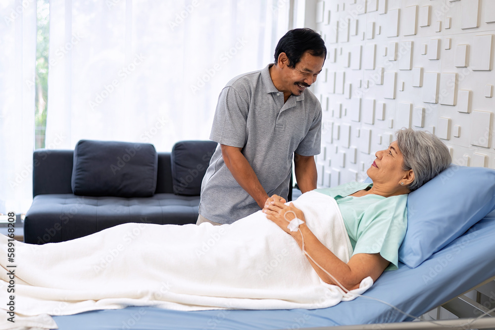 Fototapeta premium Relatives husband visiting senior wife lady talking together laying on bed during hospital stay