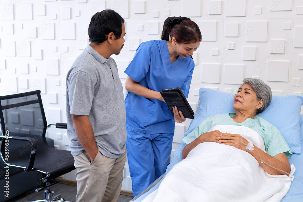 Nurse showing medical insurance data in digital tablet near bed of patient with relative stand by Nurse showing medical insurance data in digital tablet near bed of patient with relative stand by