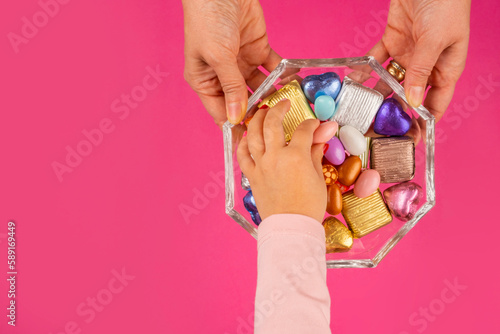 Sugar feast concept, top view image of sugar feast concept. Woman hands holding glass sweet bowl, kid hand taking one of the almond dragee. Traditional Turkish Ramazan or ramadan festive holiday. photo