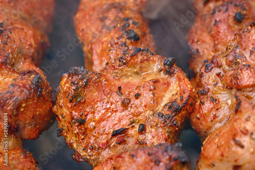 Roasted meat cooked at barbecue, closeup. Juicy piece of grilled meat with crisp crust. Spicy marinated meat cook on bbq grill. Pork meat, shashlik, prepared on grill outdoor.