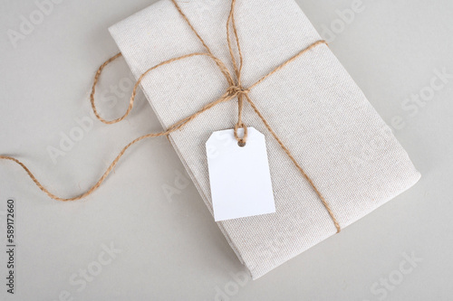 Tag mockup on folded cotton fabric, new beige clothes with blank clothes tag on white background