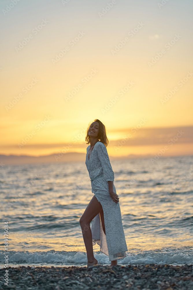 Attractive young elegant lady in dress enjoying sunset time at the beach. Background orange sundown on the sea Attractive young elegant lady in dress enjoying sunset time at the beach. Background orange sundown on the sea