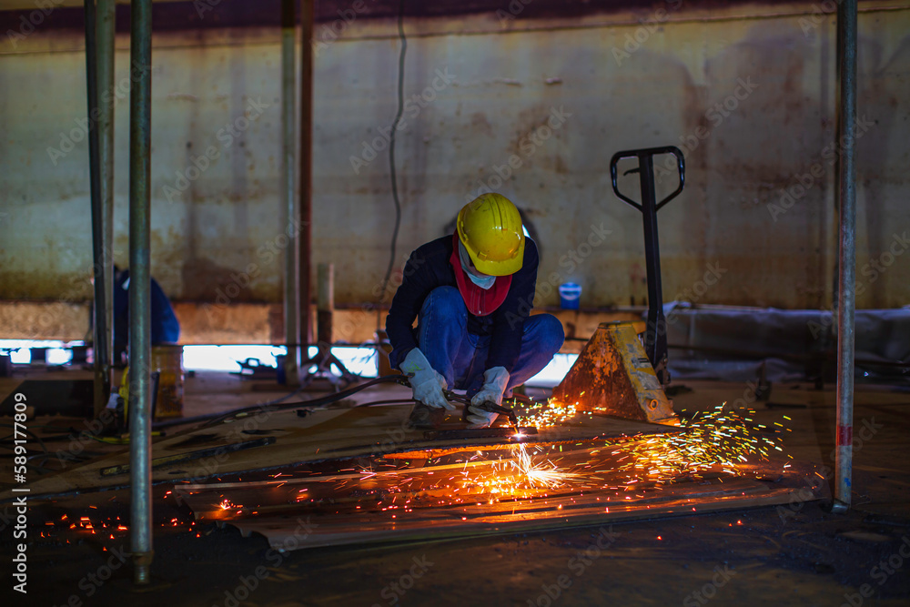 Male worker metal cutting spark on tank bottom steel plate with flash of cutting light close up wear protective gloves and mask Male worker metal cutting spark on tank bottom steel plate with flash of cutting light close up wear protective gloves and mask