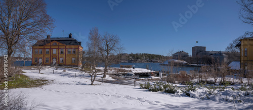 Old wood apartment house on a ness and the fortress Vaxholms fästning, melting snow, a sunny spring day in Stockholm