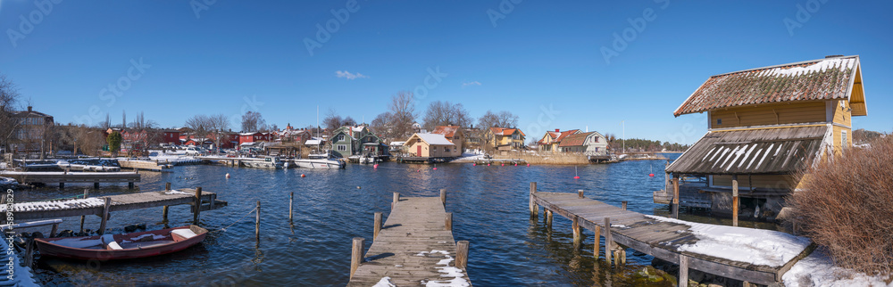 Obraz premium Cliffs and jetty houses at the bay Norrhamnen in the island Vaxholm, melting snow, a sunny spring day in Stockholm