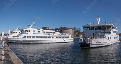 Commuter archipelago ferries moored at a pier in the archipelago town Vaxholm one ferry arrives, famous fortress and hotel, a sunny spring day in Stockholm
