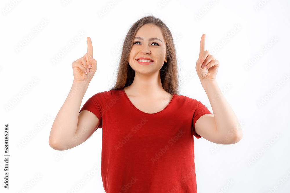 Smiling lovely girl points fingers up, shows advertisement on blank white space. Young brunette female looking happy by promotion offer, stands over white background Smiling lovely girl points fingers up, shows advertisement on blank white space. Young brunette female looking happy by promotion offer, stands over white background