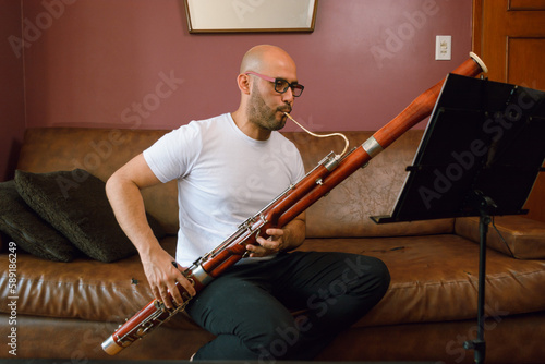 Fotografie young latin man sitting playing the bassoon, reading and studying sheet music at