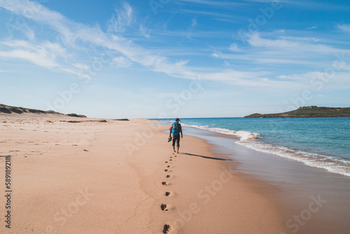 Passionate backpacker, backpack and boots in hand, walks along the Praia da Ilha do Pessegueiro beach on the Atlantic Ocean near Porto Covo, Portugal. In the footsteps of Rota Vicentina photo
