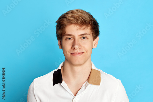 Portrait of young man, student in casual clothes posing with smiling, positive face against blue studio background. Feeling confident. Concept of emotions, youth, facial expression, lifestyle © master1305
