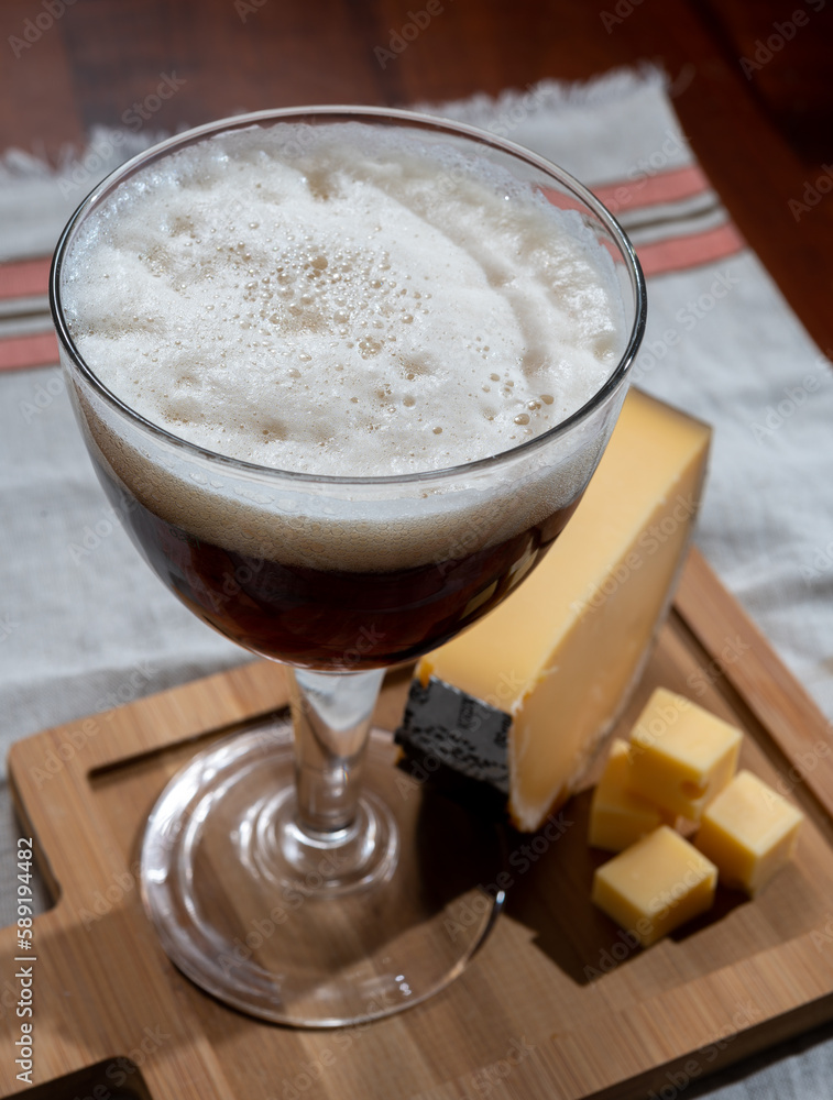 Glass of Belgian abbey brown beer and wooden board with old belgian cheese made by monks from cow milk