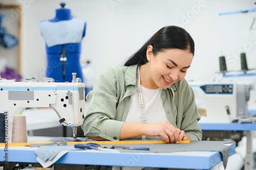 Young dressmaker woman sews clothes on working table. Smiling seamstress and her hand close up in workshop.