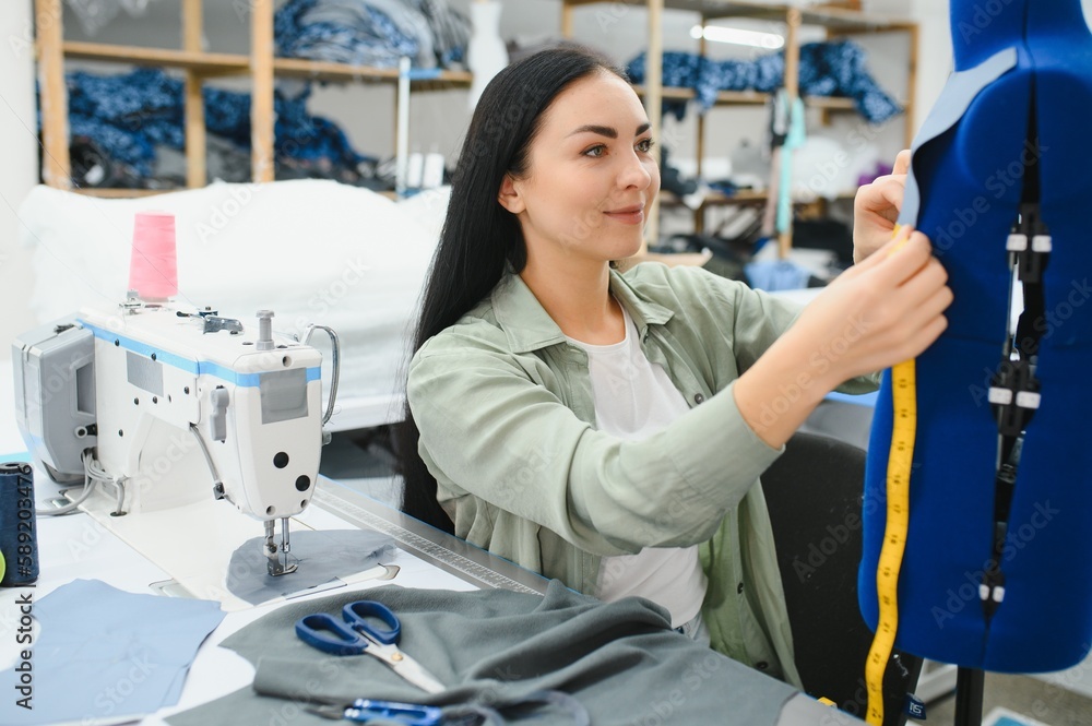 Happy female dressmaker working with sewing machine at textile factory. Happy female dressmaker working with sewing machine at textile factory.