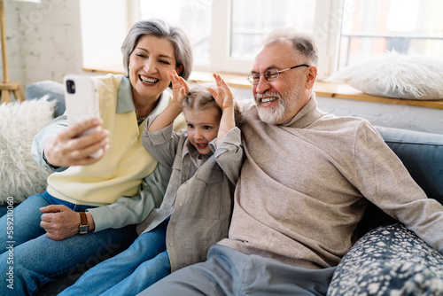 Happy senior couple sitting with granddaughter and taking selfie