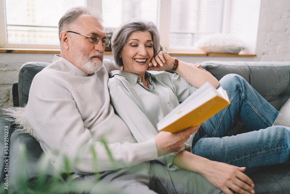Happy senior woman reading book and smiling while sitting together with husband