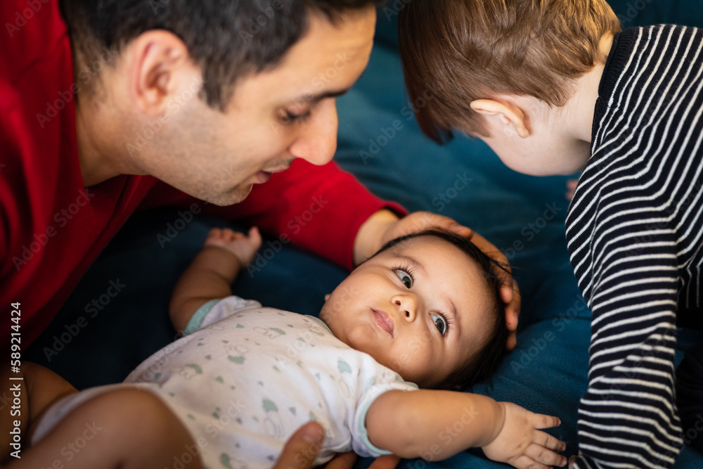 Father and two children. Family. The newborn lies on the bed, the father and elder brother are looking at him. Father and two children. Family. The newborn lies on the bed, the father and elder brother are looking at him.