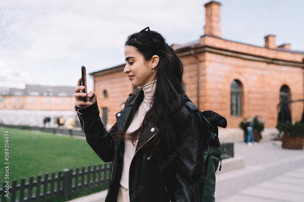 Naklejka premium Cheerful young woman taking photo on smartphone