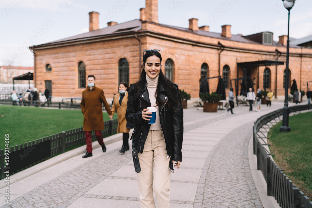 Fototapeta premium Cheerful woman with takeaway coffee walking on street