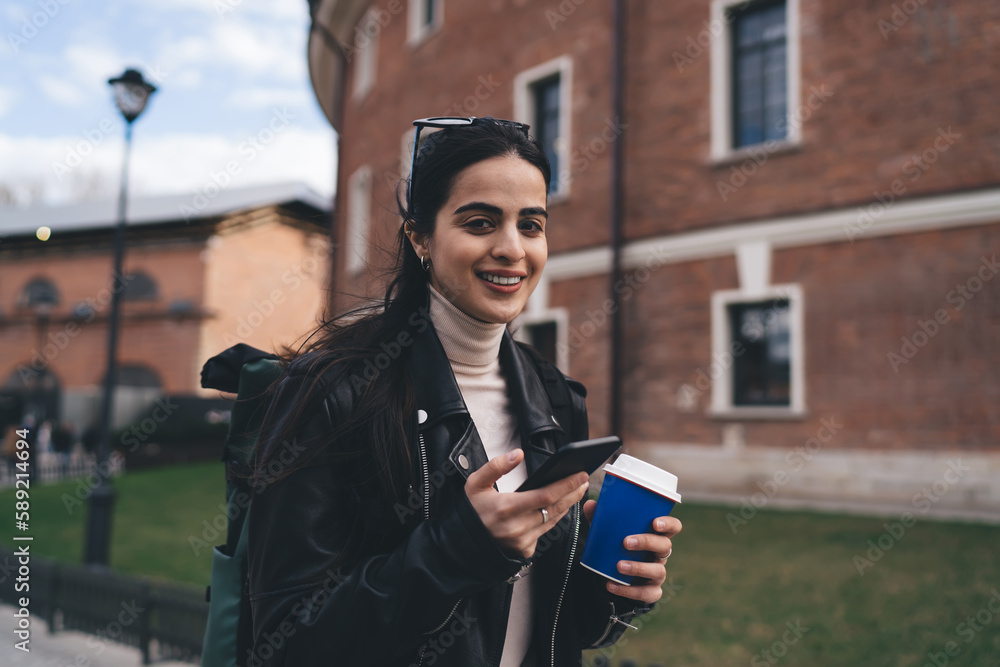 Positive woman enjoying walk with smartphone and coffee