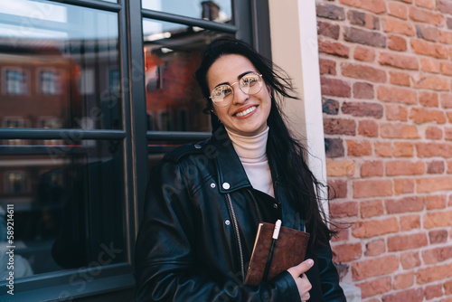 Cheerful woman standing with notepad pen in hand near window