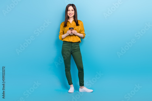 Full length photo of cheerful shiny lady dressed yellow shirt communicating modern gadget isolated blue color background