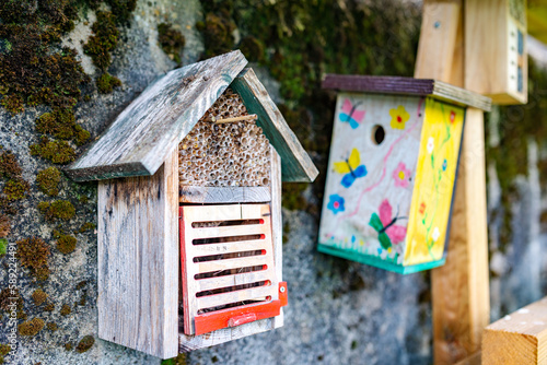 A wooden insect house or insect hotel with a bird house in the background