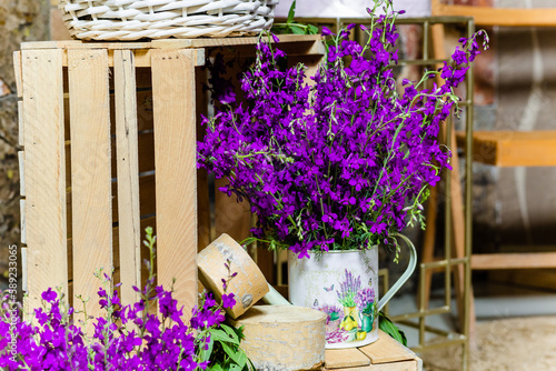 Close-up of lavender flowers in decorative watering can on floor decorated with wooden boxes © Vardan