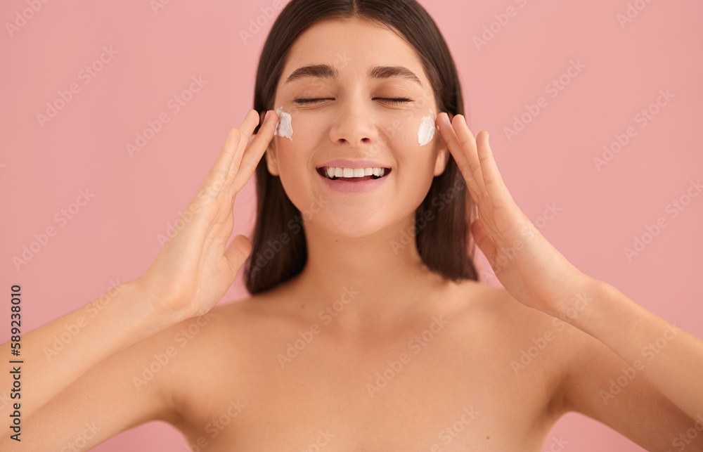 Smiling woman applying cream on face Smiling woman applying cream on face