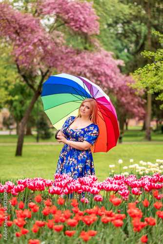 girl in a bright blue dress with a rainbow umbrella on a background of pink and yellow tulips in a spring park photo