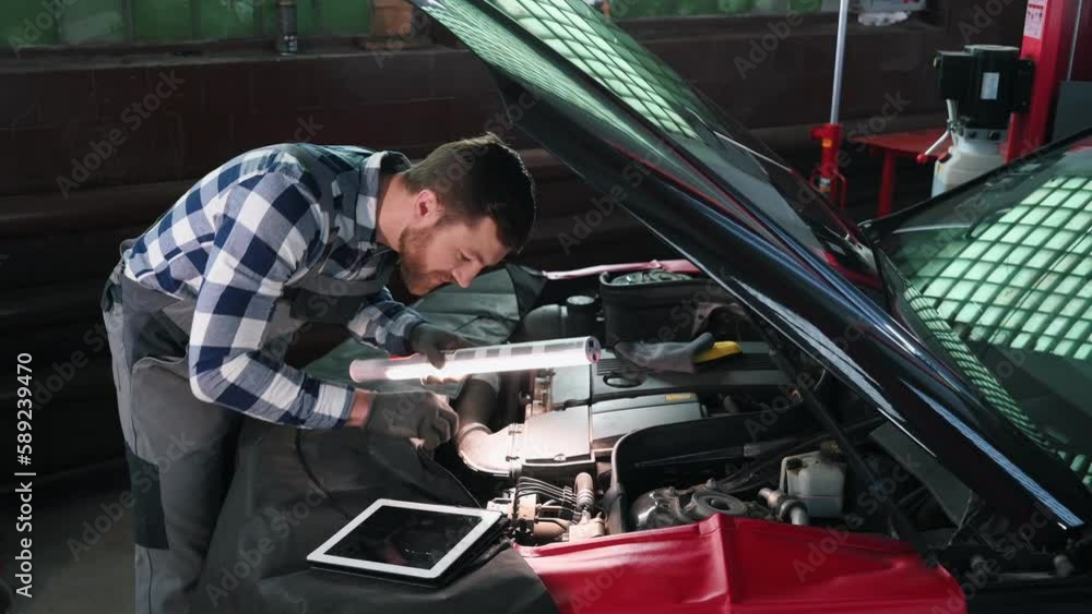 Looking at under the hood. Man is repairing the car at a service station. Looking at under the hood. Man is repairing the car at a service station.